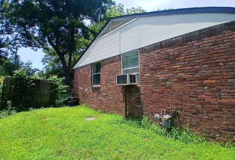 Brick exterior with white siding above, featuring a window and an attached air conditioning unit