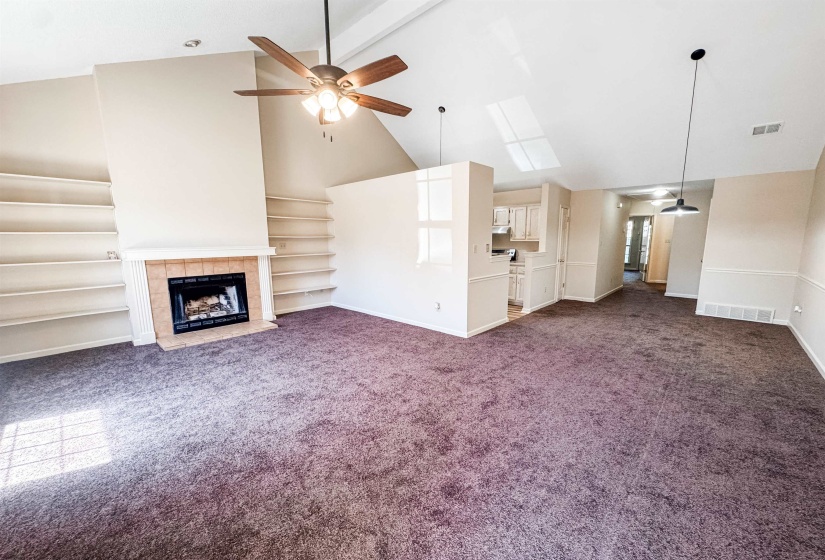 Vaulted ceilings enhance this living area featuring a fireplace with a tiled surround, built-in shelving, a ceiling fan, and pendant lighting