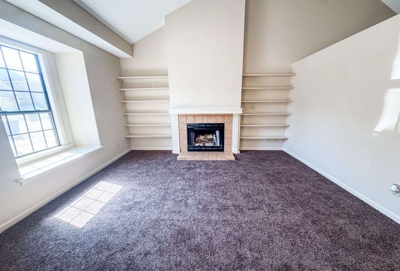 Living area featuring a fireplace with a tile surround and hearth, built-in shelving, vaulted ceilings, and a window with a deep sill