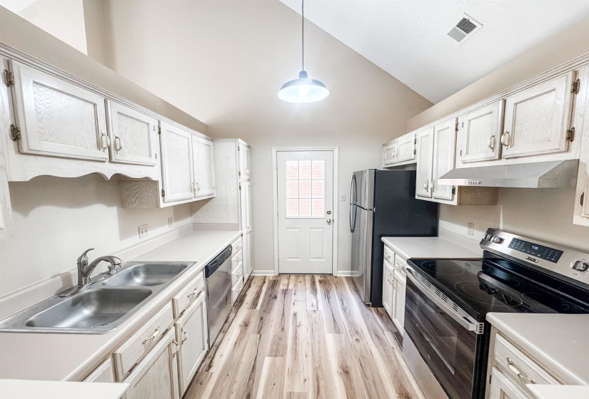 Kitchen featuring white cabinetry, wood-finish flooring, stainless steel appliances, a double basin sink, and a vaulted ceiling