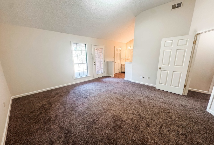 Spacious interior room featuring vaulted ceilings, plush brown carpeting, and light-toned walls