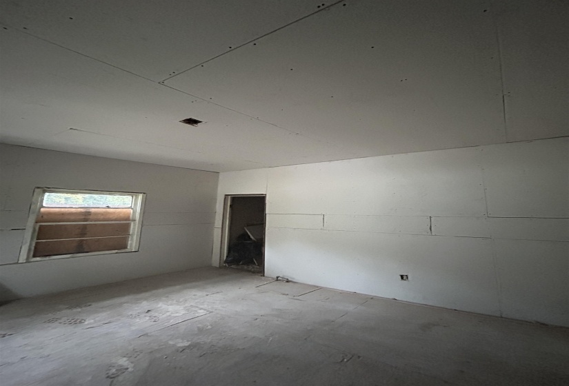 Room with partial drywall installation, raw concrete flooring, and a window opening