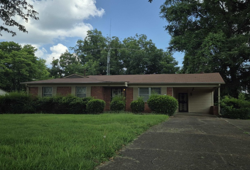 Brick exterior featuring a covered carport, mature front lawn, and established landscaping
