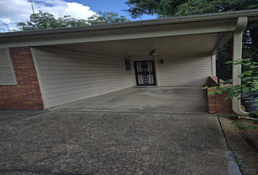 Covered carport with concrete flooring, brick accents, and a security screen door