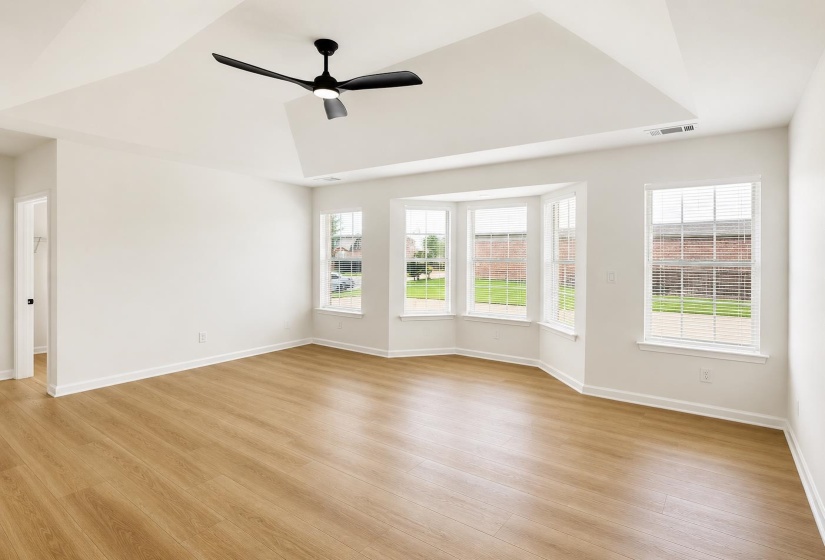 Spacious room featuring a tray ceiling, contemporary ceiling fan, and wood-finish flooring