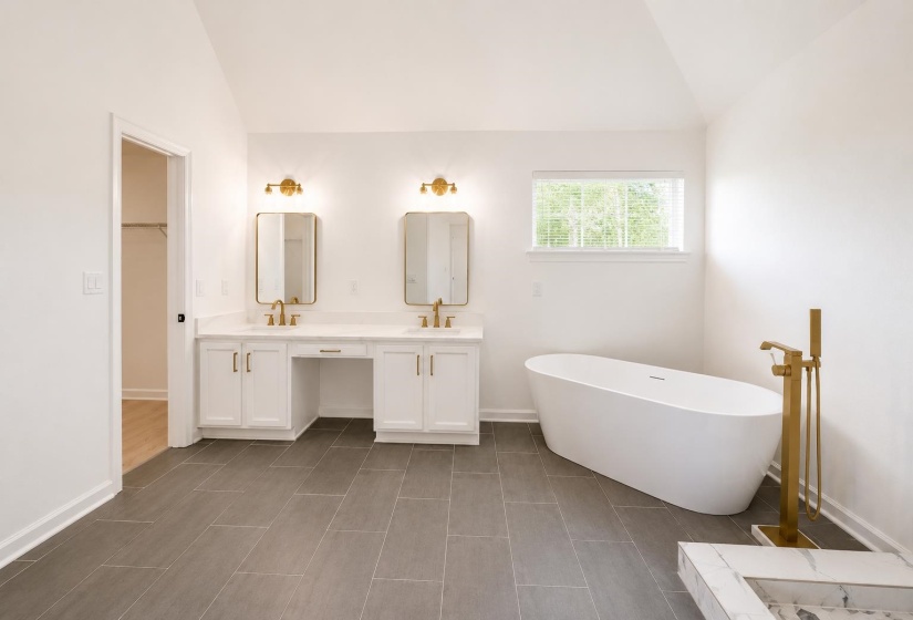 Spacious bathroom featuring a freestanding tub with a gold-tone floor-mounted faucet, a dual vanity with white cabinetry and gold-tone hardware, and rectangular mirrors with sconce lighting