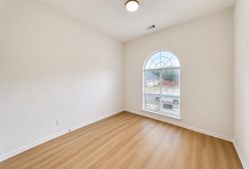 Bright room featuring an arched window with grid patterns, light wood-finish flooring, white baseboards, and a flush-mount ceiling light fixture