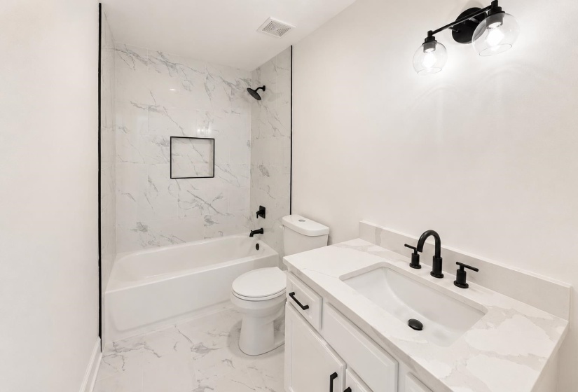 Bathroom featuring a white bathtub with a tile surround, a built-in shower niche, and matte black fixtures
