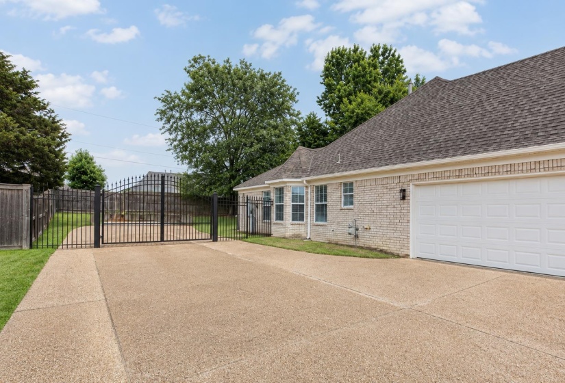 Concrete driveway with an integrated wrought iron gate, leading to a brick exterior residence featuring a two-car garage and multiple windows