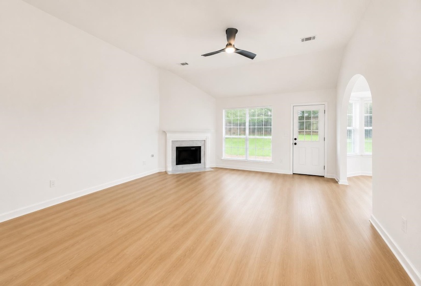 Spacious room featuring wood-finish flooring, a corner fireplace with a white mantel, and a ceiling fan