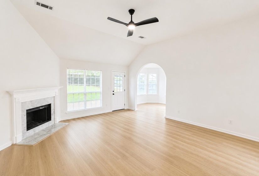 Vaulted ceiling living space featuring wood-finish flooring, a white mantel fireplace with a stone surround, and an arched doorway leading to an additional space with bay windows