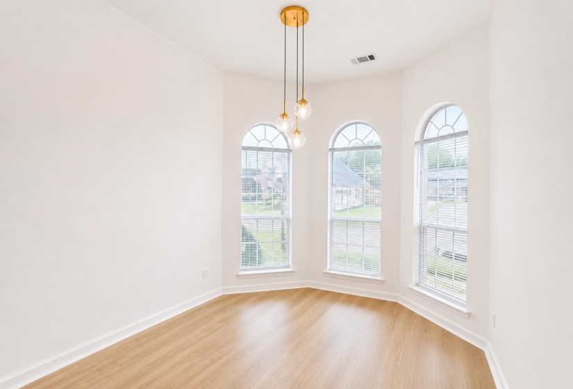 Room featuring three arched windows, wood-finish flooring, a contemporary multi-globe pendant light fixture with a gold-tone base, and white baseboards