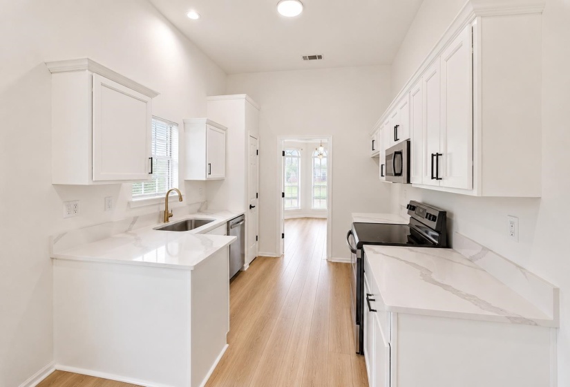Kitchen featuring white cabinetry with black hardware, light-toned wood-finish flooring, and white countertops with subtle gray veining