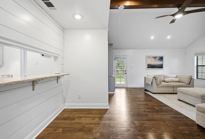 Spacious living area featuring wood-finish flooring, vaulted ceilings with exposed beams, and a modern ceiling fan