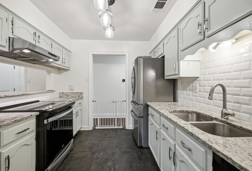Kitchen featuring light grey cabinetry, stone countertops, stainless steel appliances, a subway tile backsplash, and dark slate-look flooring