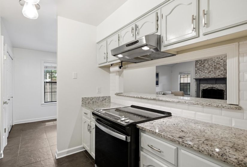 Kitchen featuring granite countertops, subway tile backsplash, white cabinetry, and a pass-through opening to an additional room