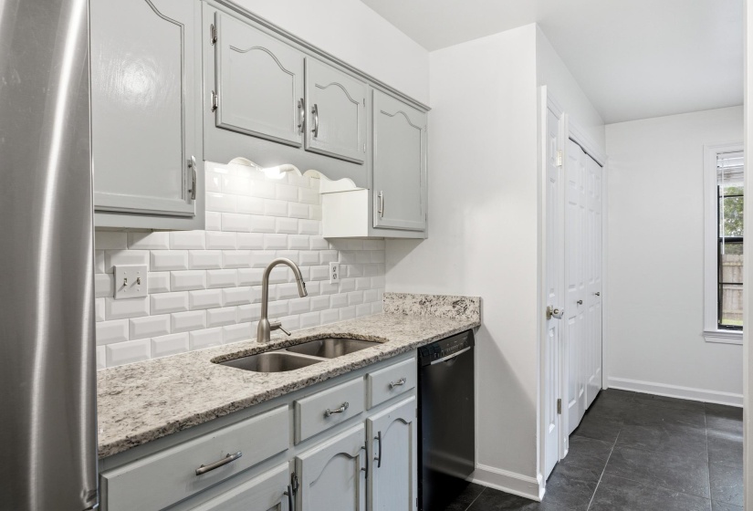 Kitchen featuring light gray cabinetry, a dual basin stainless steel sink with a gooseneck faucet, light-toned stone countertops, and a white subway tile backsplash