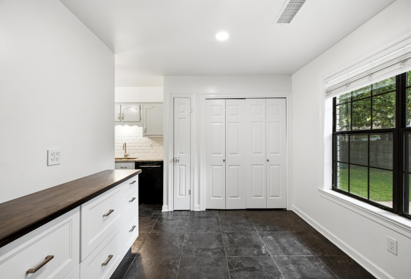Spacious room featuring dark tile flooring, a large window with white blinds, a built-in storage unit with a wood-finish countertop, and bi-fold closet doors
