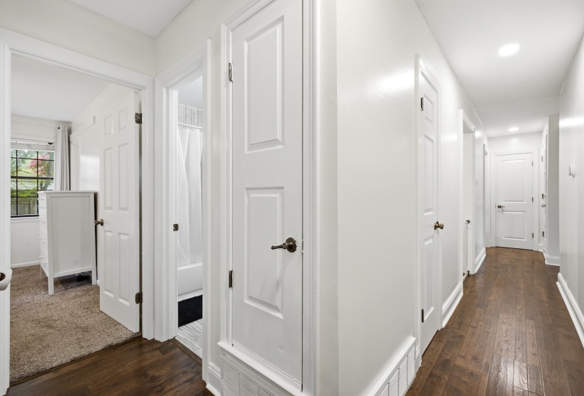 Hallway featuring wood-finish flooring, white panel doors with dark hardware, and recessed lighting