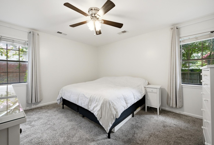 Bright bedroom featuring a ceiling fan with integrated lighting, two windows with white trim, and light gray carpet flooring