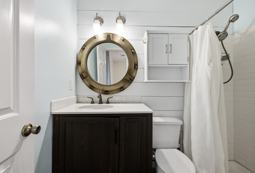 Bathroom featuring a dark wood-finish vanity with a white countertop, a circular porthole-style mirror, and a wall-mounted medicine cabinet with open shelving