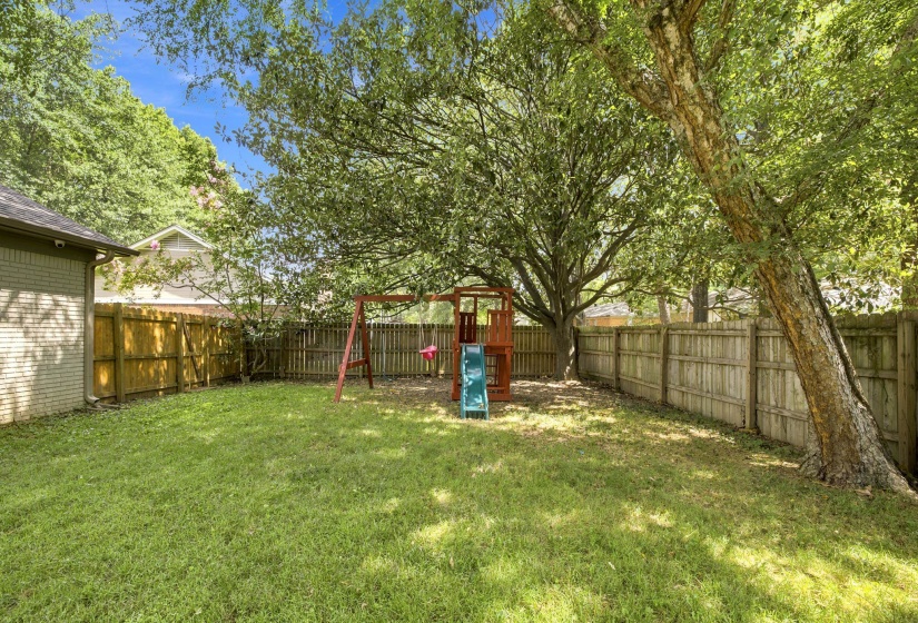 Expansive grass lawn featuring a wood privacy fence, mature trees, and a visible brick exterior on a portion of the property's structure