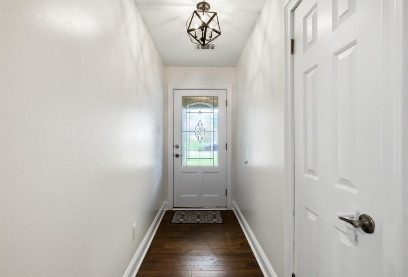 Entryway featuring wood-finish flooring, white baseboards, a white paneled door with a bronze lever handle, and a white front door with leaded glass