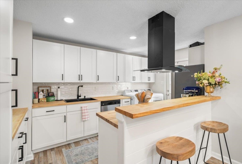 Kitchen featuring white cabinetry, light wood-finish countertops, a white subway tile backsplash, a black sink with a black faucet, and a black range hood