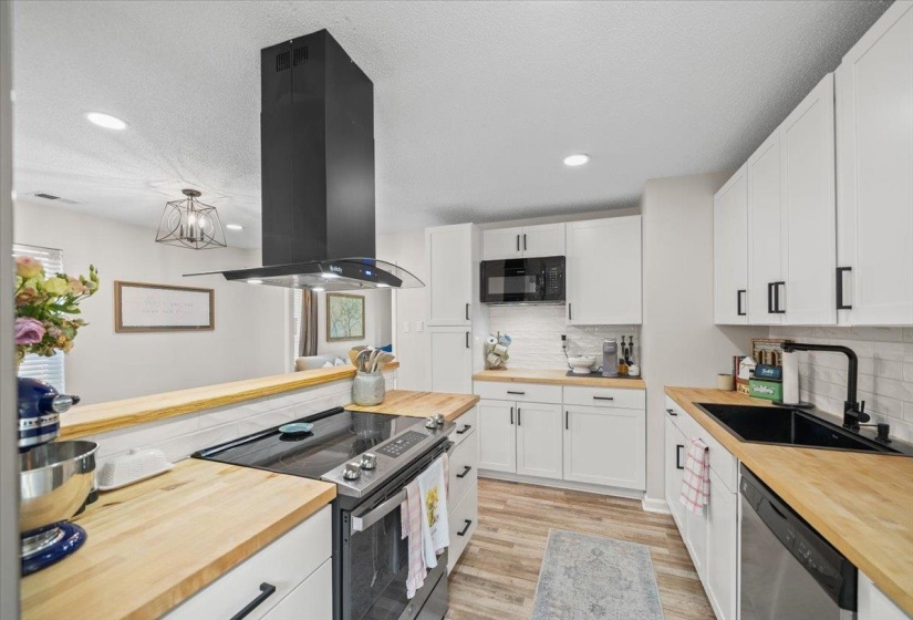 Modern kitchen featuring white cabinetry, butcher block countertops, stainless steel appliances, and a black range hood