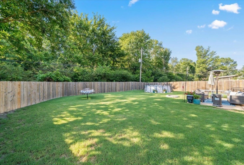 Spacious backyard featuring a manicured lawn, a full privacy fence, and a dedicated patio area