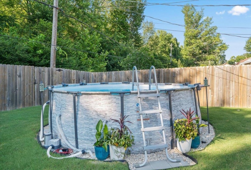 Above-ground pool featuring a stone-look exterior, surrounding gravel landscaping, and a wooden privacy fence