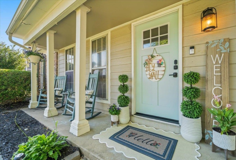 Covered porch with square support columns, light siding, and a light blue entry door featuring upper window panes