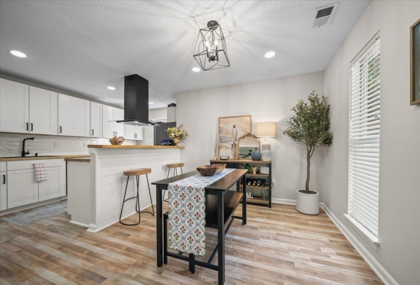 Kitchen and dining area featuring wood-finish flooring, white cabinetry with black hardware, a black range hood, a shiplap-paneled breakfast bar with a wood countertop, and recessed lighting