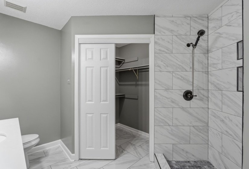 Spacious bathroom featuring a walk-in shower with large format tile and black fixtures, bifold closet door, and tile flooring