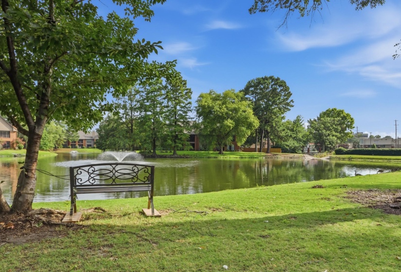 Serene pond with a central water feature, surrounded by mature trees and manicured green space