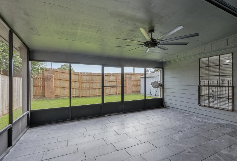 Screened patio featuring large format rectangular tile flooring, a dark multi-blade ceiling fan, and a wood fence enclosing the backyard