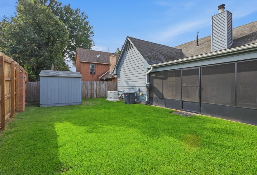 Expansive green lawn with a screened-in patio, wood privacy fencing, and a detached storage shed