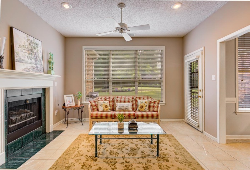 Living area featuring a fireplace with a white mantel and green stone surround, a large window, a glass-paned door, recessed lighting, and a ceiling fan