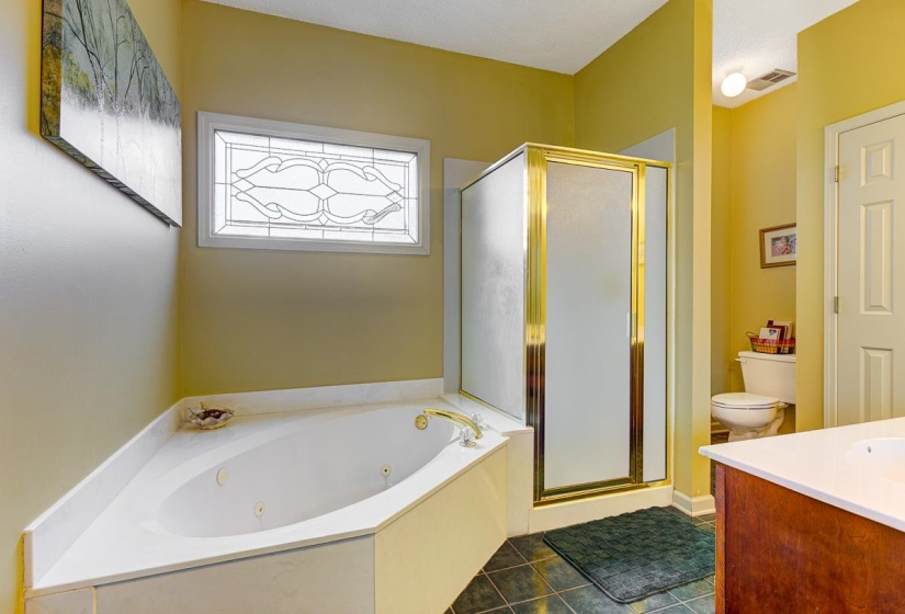 Corner jetted tub with gold-tone fixtures and an overhead decorative frosted window