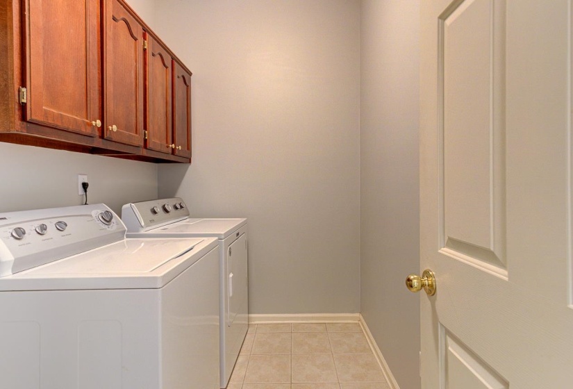 Laundry area featuring upper wood cabinetry with gold-tone hardware, a light tile floor, and baseboard molding