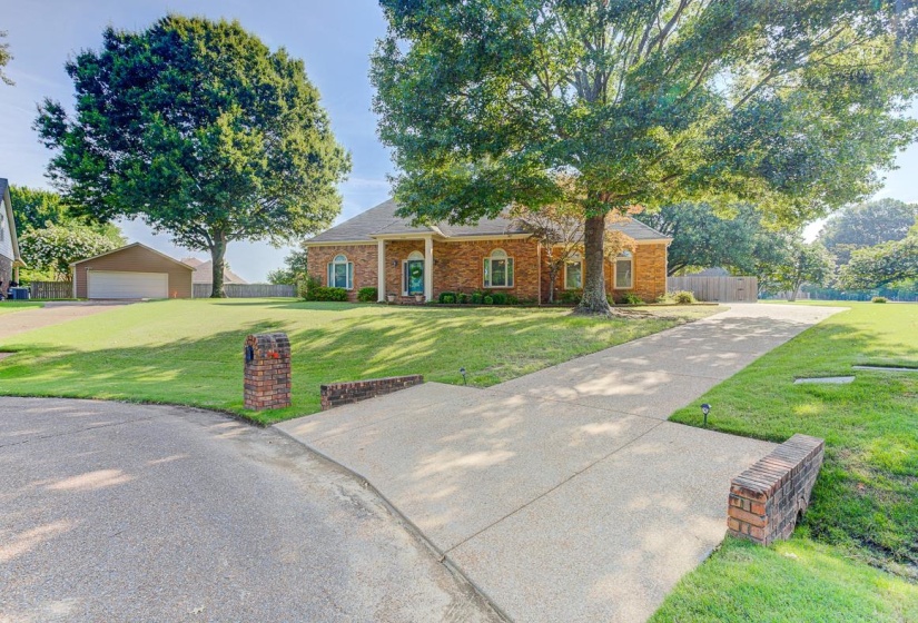 Brick exterior residence with a deep front yard, mature trees, and a concrete driveway