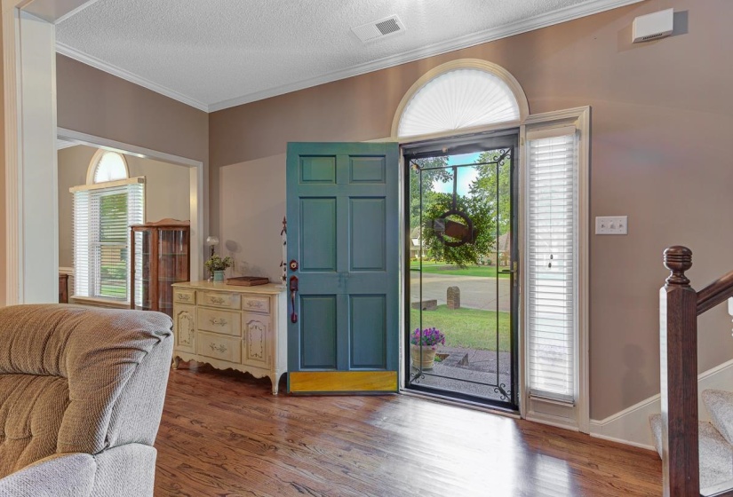 Entryway featuring wood-finish flooring, a teal panel door, an arched transom window, a sidelight window with blinds, and white crown molding