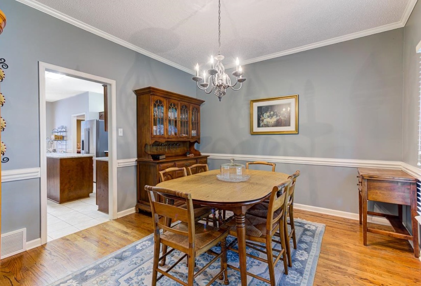 Dining area featuring wood-finish flooring, crown molding, chair rail molding, and a chandelier light fixture