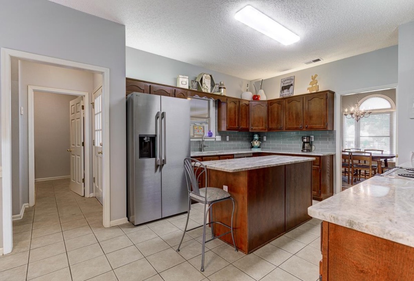Kitchen featuring wood cabinetry, light-toned tile flooring, and a central island with a stone countertop