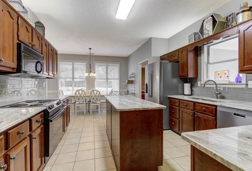 Kitchen featuring wood cabinetry, light-colored countertops, stainless steel appliances, and a tiled backsplash