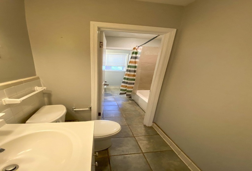 Bathroom featuring a white vanity with integrated sink, white toilet, and gray tile flooring