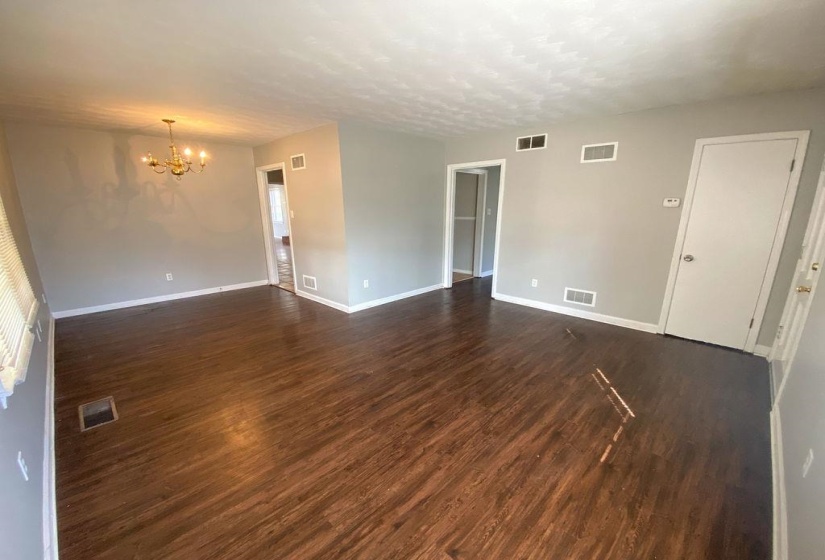 Open concept living area featuring dark wood-finish flooring, light gray walls, white baseboards, and a brass chandelier
