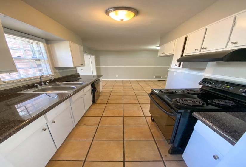 Galley kitchen featuring tile flooring, white cabinetry, dark countertops, a double basin sink, and a black electric range