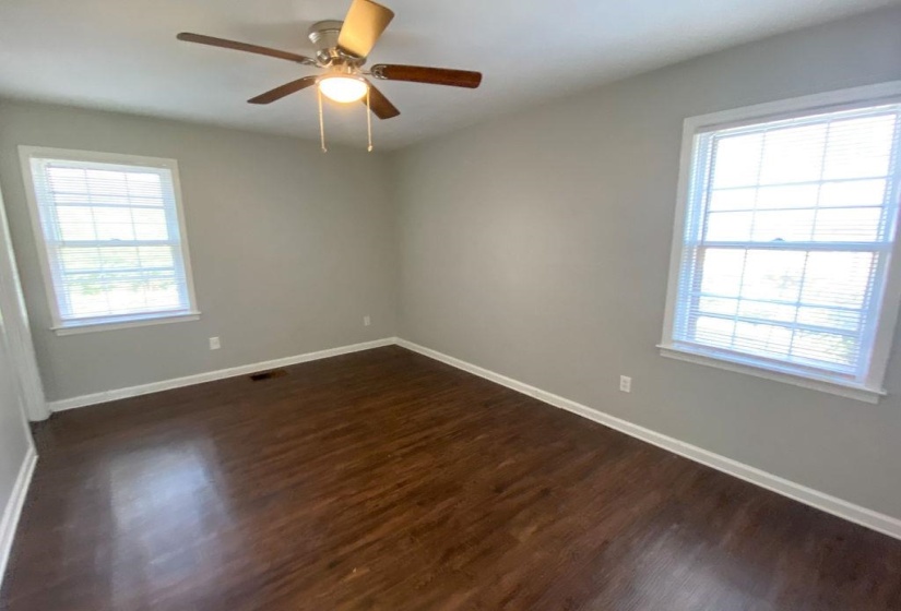 Interior room featuring wood-finish flooring, two large windows with blinds, a ceiling fan with integrated lighting, and neutral wall paint