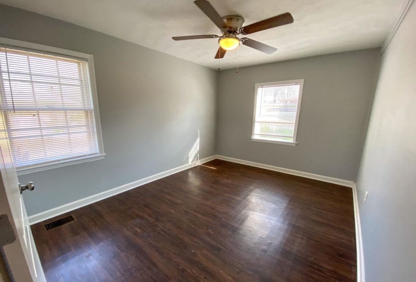 Room with wood-finish flooring, two window openings, a ceiling fan with light fixture, and white baseboards